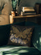 A black woven throw pillow featuring an embroidered gold Hamsa hand surrounded by intricate floral and botanical designs.